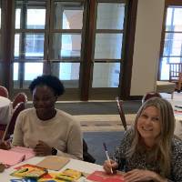 Two women from SSW sitting at a table decorating lunch bags for Kids' Food Basket